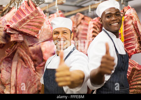 cheerful butchers giving thumbs up in cold room Stock Photo
