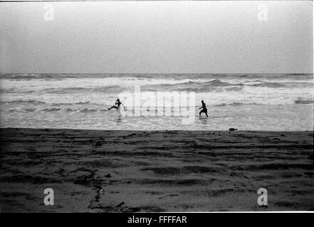 Jan 4, 2016 - South Beach, KwaZulu-Natal, South Africa - Two men running in the waves. South Beach is a part of the City of Durban's longest uninterrupted stretch of beach sand. The City of Durban is on the eastern seaboard of South Africa and the people here are washed with the warm waters of the Indian Ocean. To the north of this stretch of sand are beaches with cafe society hang outs. To the south there is a pier with the upmarket Moyo's Restaurant at it's end and the uShaka Marine World complex and the private surf and sea clubs of the Vetches Beach area. Between these northern and souther Stock Photo