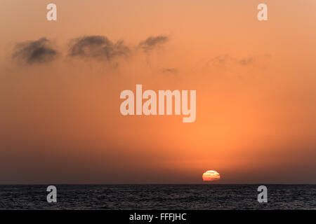 Rising sun partially hidden with clouds from behind the sea Stock Photo