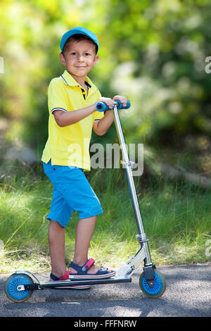 Smiling boy riding a scooter in the park. Stock Photo