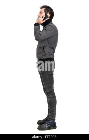 Side view of young bearded man in gray jacket talking on the mobile phone. Full body length portrait isolated over white Stock Photo