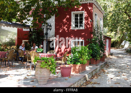 Shaded by an old Plane tree, three elderly gentlemen enjoy an afternoon beer outside a traditional Greek village home. Stock Photo