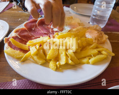 woman hand taking dish with typical Spain food fried eggs with potatoes french fries eggs and iberico iberian ham Stock Photo