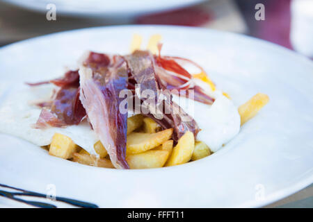 still life of white dish typical Spain food fried eggs with potatoes french fries fried eggs and slices of iberico ham on table Stock Photo