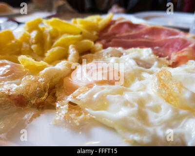 macro of white dish with typical Spain food fried eggs with potatoes french fries fried eggs and slices of iberico iberian ham Stock Photo