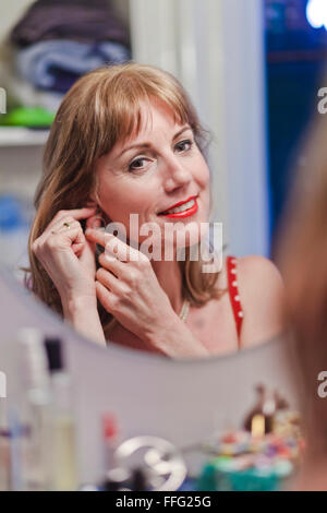 Mature woman putting on earring. Stock Photo