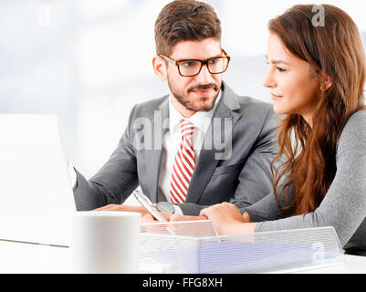 Image of young businessman sitting in front of laptop and giving advise to sales woman. Business people consulting at office. Stock Photo
