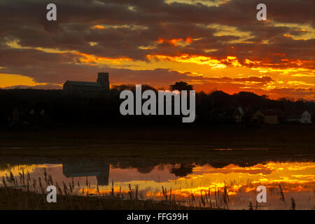Salthouse Village church and flooded marshes in foreground at sunset Stock Photo
