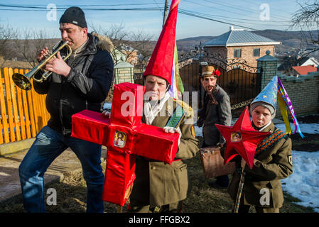 Koliadnyky - group of adult and kids dressed in costumes of soldiers and traditional Ukrainian female costumes – hold red cross and a star, christian and pagan symbols of Malanka celebration in Velykyj Kuchuriv village, Bukovina, Ukraine Stock Photo