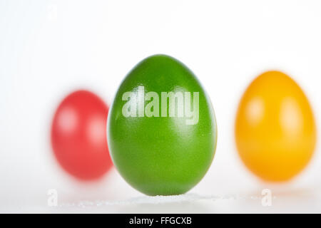 Three colored easter eggs standing on a white background on little pile of salt