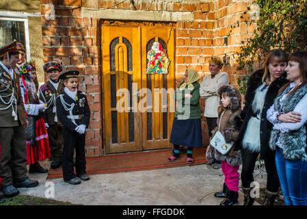 Koliadnyky - group of adult and kids dressed in costumes of soldiers and traditional Ukrainian female costumes - sing carols (koliadky) during Malanka celebration in Velykyj Kuchuriv village, Bukovina, Ukraine Stock Photo