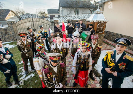 Koliadnyky - group of adult and kids dressed in costumes of soldiers and traditional Ukrainian female costumes - sing carols (koliadky) during Malanka celebration in Velykyj Kuchuriv village, Bukovina, Ukraine Stock Photo