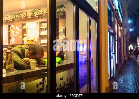 Lonely man falling asleep at a cafe at night as seen from the street Stock Photo