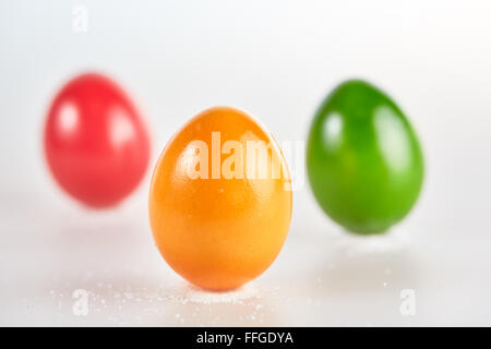Three isolated colored easter eggs standing on little piles of salt on white background