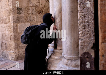 An Orthodox Christian pilgrim kissing the columns which are covered in crusader graffiti mostly consisting of crosses at the entrance to the Holy Sepulchre church in Christian Quarter old city East Jerusalem Israel Stock Photo