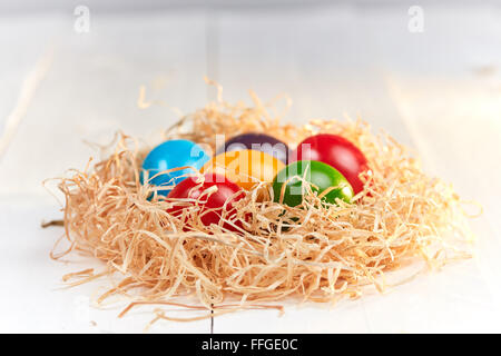 Six easter eggs with different colors in an easter nest of straw on a white wooden table. Stock Photo
