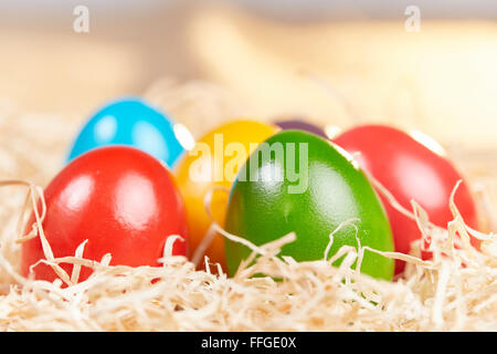 Closeup of six different colored easter eggs in a nest of hay with sunlight in the background. Stock Photo