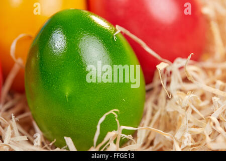 Macro closeup of green easter egg in a nest of hay with a red and a yellow egg in the background Stock Photo