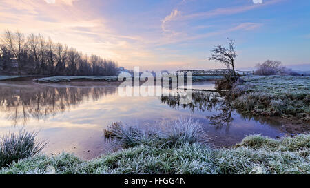 Cold frosty morning looking across the river stour with footbridge on Sudbury meadows, Suffolk, England. Stock Photo