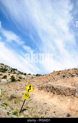 Speed limit sign on a curvy, rocky road with blue sky and clouds Stock Photo
