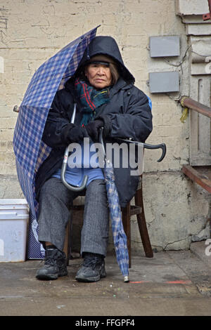 Portrait of an elderly Chinese woman with two umbrellas on Chinese New Year's day on Mulberry Street in Chinatown, New York City Stock Photo