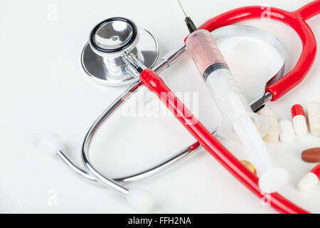 Red stethoscope with a hypodermic syringe and some pills laying on a medical work surface Stock Photo