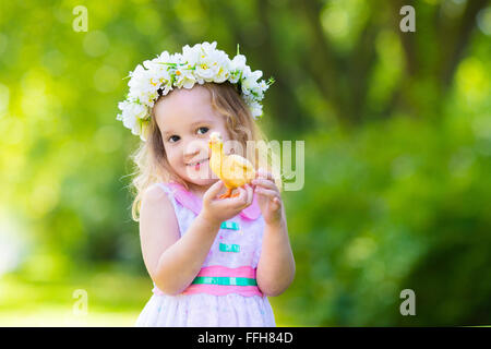 Little girl having fun on Easter egg hunt. Kid in flower crown playing with toy duck or chicken. Children searching for eggs Stock Photo