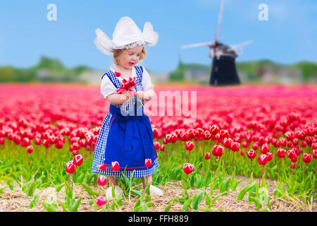 Adorable curly toddler girl wearing Dutch traditional national costume dress and hat playing in a field of blooming tulips Stock Photo