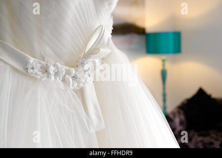 A traditional white wedding dress hanging in a bedroom waiting for a bride to put it on Stock Photo