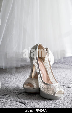 A brides shoes sit crossed, below her dress on carpet waiting to be worn during the wedding day Stock Photo