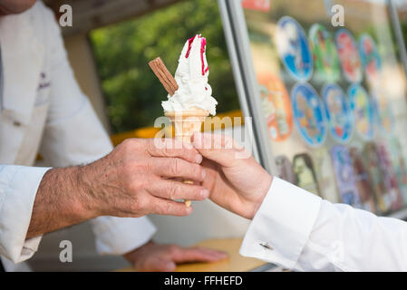An ice cream sales man handing over a 99 whipped ice cream cornet from a van Stock Photo