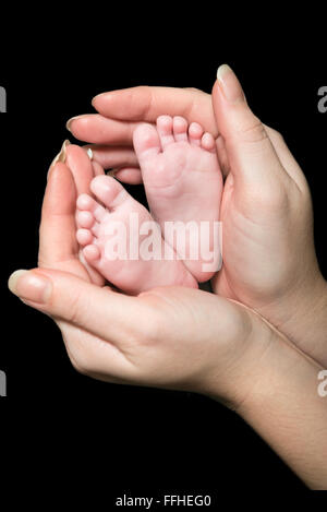 An image of the crossed feet of a newborn with wedding rings on its toes, cupped in its mothers hands Stock Photo