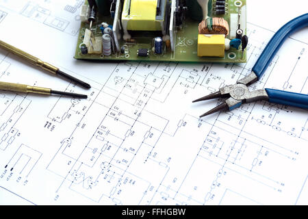 Printed circuit board with electrical component and precision tools lying on construction drawing of electronics. Stock Photo