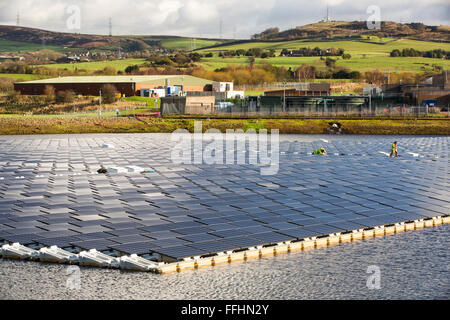 The new floating solar farm being grid connected on Godley Reservoir in Hyde, Manchester, UK. The scheme is a 3 MW system, comprising of 10,000 photo voltaic panels. It will cut United Utilities electricity bill at the water treatment plant on site, by around £7,000 a month. It is the largest floating solar farm in Europe and the second largest in the world. It will provide around 33% of the water treatment plants energy needs. Stock Photo