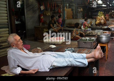 Elder lying and sleeping on a tatami in a Market stall and street food being prepared in Chinatown Bangkok, Thailand. Yaowarat, Stock Photo