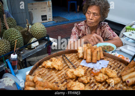 Woman selling pring rolls and durian fruits. Bangkok's Chinatown , Thailand. Market stall and street food being prepared in Chin Stock Photo