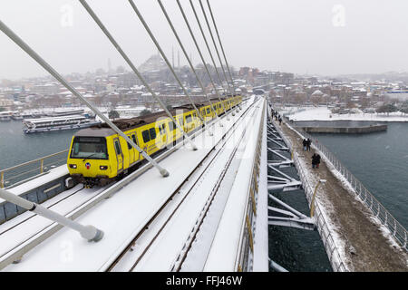 Istanbul subway metro train passing and people walking on the Golden Horn Metro Bridge on a snowy day near Halic in Istanbul Stock Photo