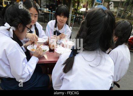 Thai High school students enjoying a bowl of Thai soup with noodles at a small street restaurant in Bangkok. Stock Photo