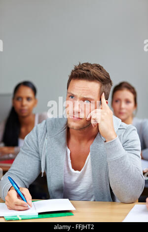 Pensive student thinking and taking notes in university class Stock Photo