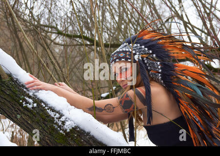 Girl in native american headdress climbs tree Stock Photo