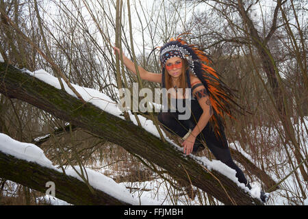 Girl in native american headdress climbs tree Stock Photo