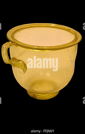 Ancient roman green glass cup from the 2nd century AD, with shaped handle. Isolated against a black background. Stock Photo