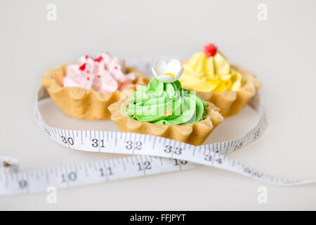 Three colorful green, pink and yellow tart cakes wrapped in measuring tape on white background, unhealthy lifestyle concept, stu Stock Photo