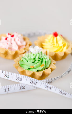 Three colorful tart cakes wrapped in measuring tape on white background, weight loss concept, studio Stock Photo