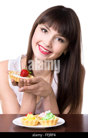 Headshot portrait of young friendly smiling woman sitting in front of plate with cream cupcakes and holding in her palm Stock Photo