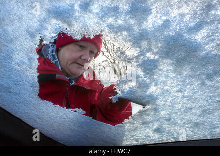 Senior woman clearing snow from the windshield of a car Stock Photo