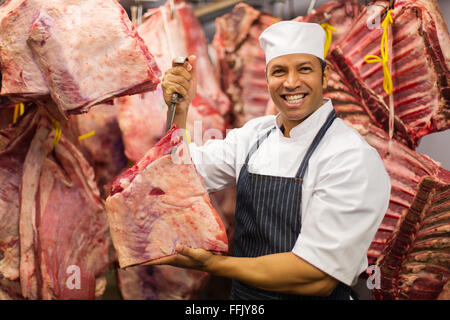 confident middle aged butcher hanging beef in cold room Stock Photo