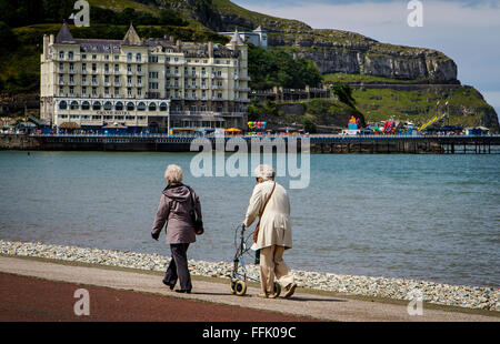 Two elderly ladies walking along the promenade at Llandudno with The Grand Hotel and The Great Orme in the background Stock Photo
