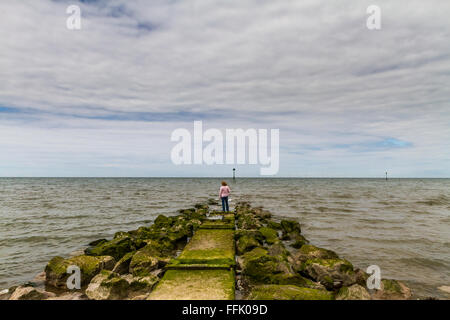 Mature lady standing at the end of a wave breaker jetty on the coastline of Colwyn Bay Stock Photo