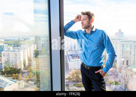 Businessman in apartment looking through window Stock Photo